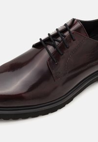Scarpa da uomo stringata in pelle bordeaux lucida, con lacci neri, cuciture a contrasto e una robusta suola in gomma nera.