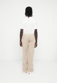 Bézs kordnadrág rugalmas derékpánttal, egyenes szárakkal és két hátsó zsebbel. Egyszerű fehér pólóval és fehér sportcipővel viselve.