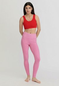 Rotes Crop-Top und pinke Leggings aus dehnbarem Stoff. Die Leggings verfügen über einen hohen Taillenbund und Nahtdetails entlang der Beine.