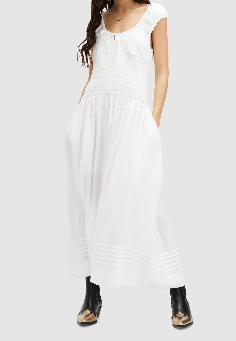 Robe maxi blanche avec un corsage smocké, des manches courtes volantées et des poches latérales, avec des détails rayés horizontaux à l'ourlet.