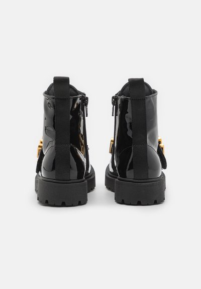 Bottines noires en cuir verni avec une finition lisse, dotées d'une fermeture éclair sur le côté, d'accents en tissu noir et d'une semelle en caoutchouc robuste.
