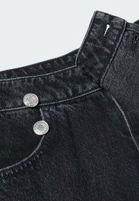 Detalle de unos pantalones vaqueros de mezclilla negra que cuentan con una cintura con botones, dos botones metálicos y una tela texturizada con costuras visibles.