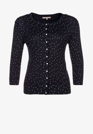 Gilet marine à pois blancs, texture tricotée, encolure arrondie et fermeture à boutons sur le devant. Manches longues avec poignets côtelés.