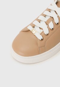 Baskets en cuir beige avec des lacets blancs, des accessoires en or, un bout arrondi et une semelle en caoutchouc blanc contrastant. Texture lisse et détails cousus.