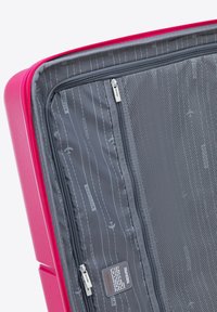 Tvrdý kufr v jasně růžové barvě; vnitřek má šedé podšívání s motivem inspirovaným letišti, zipové přihrádky a síťovou kapsu.