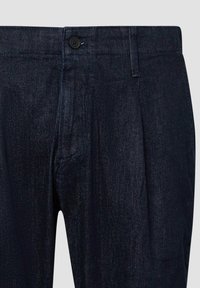 Pantaloni in denim scuro caratterizzati da una parte anteriore piatta, tasche laterali e una chiusura a bottone singolo in vita. Tessuto liscio e leggermente testurizzato.