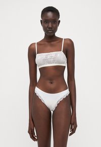 Hvit undertøysett med en gjennomsiktig bralette dekorert med blomster og matchende truser med blondekant og glatt finish.