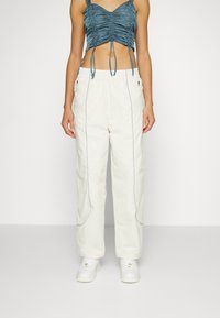 Vita löst sittande byxor med kontrasterande blå sömmar och sidofickor, kombinerat med en rynkad ljusblå croptop. Vita sneakers.