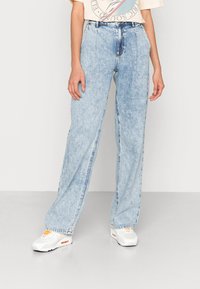 Jeans de cintura alta e perna larga em azul claro, feitos de denim, com um acabamento desgastado, bolsos frontais e detalhes de costura visíveis nas costuras.