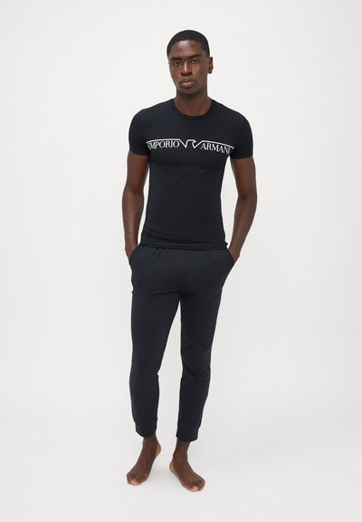 Melna kokvilnas T-kreklu ar baltu "Emporio Armani" logotipu uz krūšu daļas, apvienots ar melniem ievelkamiem jogger biksēm. Vienkāršs, pieguļošs dizains.