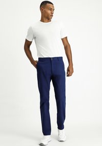 Pantalones azul marino de corte ajustado, con cierre de botón, bolsillos laterales y una textura suave. Combinados con una camiseta básica de manga corta blanca.