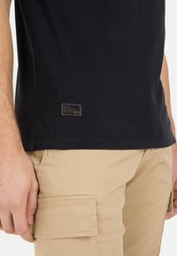 Mørkeblå bomulds t-shirt med lige kant, der har et lille rektangulært mærke med tekst. Beige cargo-bukser med sidelomme-detalje.