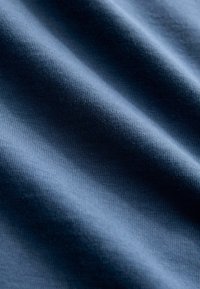 Tissu bleu foncé présentant une surface lisse, légèrement texturée avec un fin côtelé, créant des plis doux et une apparence fluide.