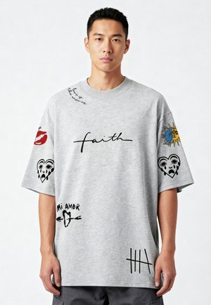 Giovane uomo che indossa una T-shirt grigia oversize con parole nere scritte a mano e grafiche di cuore, sole, labbra, e frasi come "faith" e "Mi Amor".