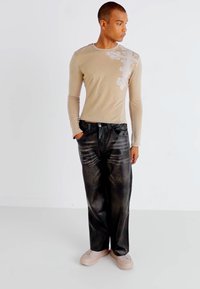 Beige long-sleeve shirt with floral pattern detailing, paired with loose-fitting black denim jeans and light-colored sneakers.