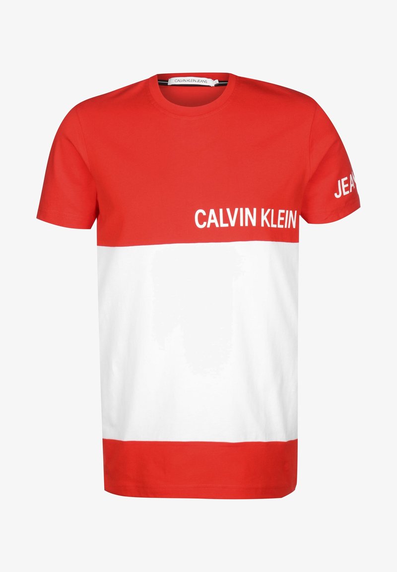 Červeno-bílý tričko s krátkým rukávem, které má na hrudi nápis "CALVIN KLEIN" a na pravém rukávu nápis "JEANS".