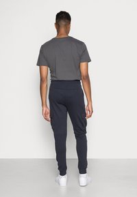 Donkergrijze katoenen T-shirt gecombineerd met marineblauwe joggers met zijcargo zakken, ribgebreide manchetten en een trekkoord in de taille. Witte sneakers gedragen.