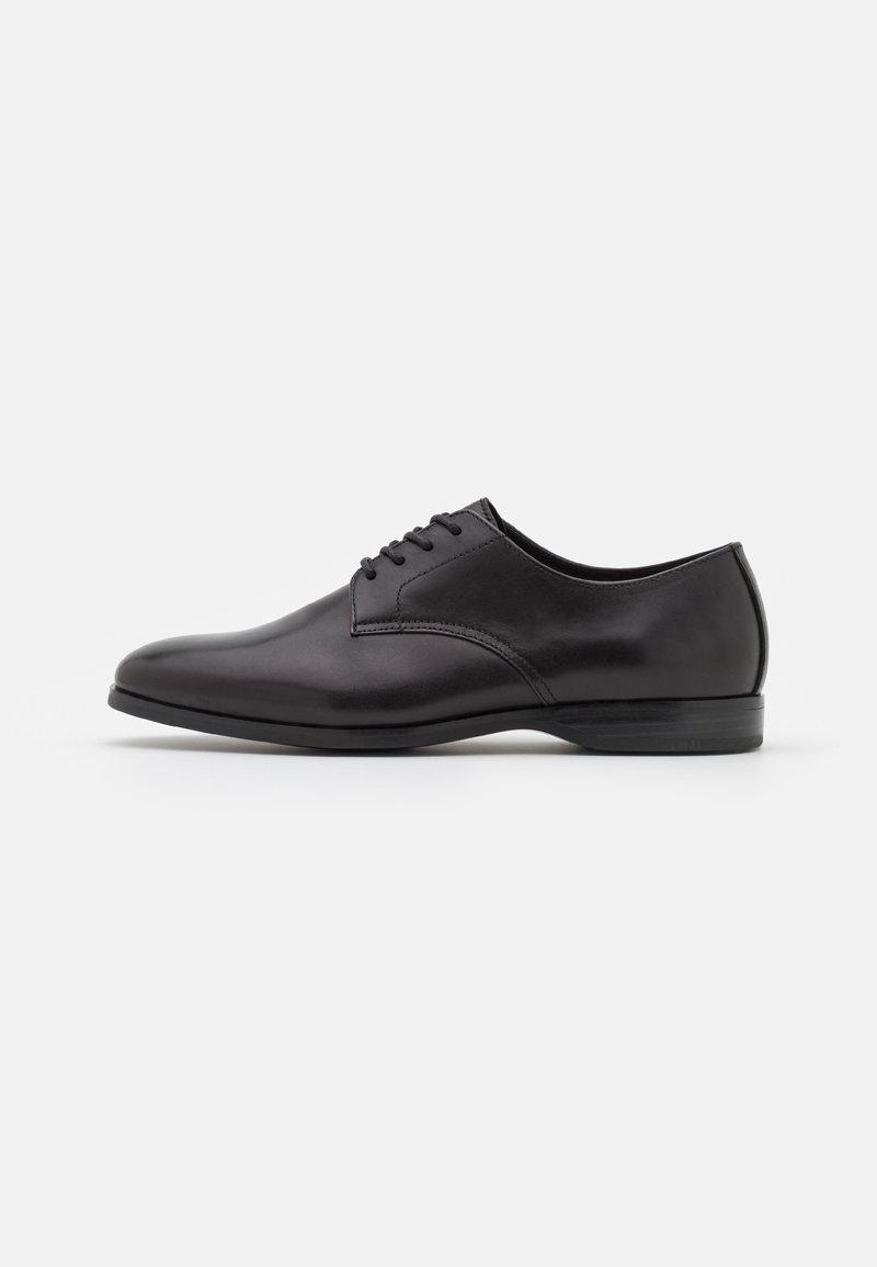 Chaussure Oxford formelle en cuir noir avec laçage fermé et talon bas, présentée en profil latéral sur fond blanc.