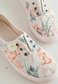Tenisky slip-on z plátna s pastelovým kvetinovým vzorom, kovovými očkami a bielymi gumovými podrážkami na svetlom povrchu.
