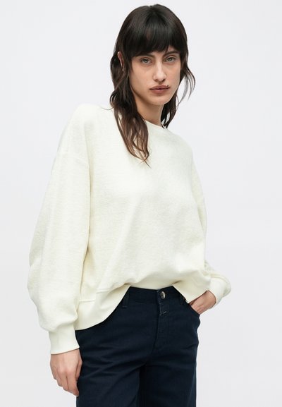 Ανοιχτό μπεζ φούτερ με υφασμάτινη υφή, ώμους με σταγόνες και ριμπ μανσέτες. Συνδυάζεται με σκούρο ναυτικό παντελόνι, με κλασική εφαρμογή.