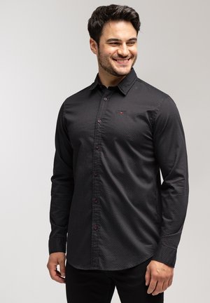 Czarna koszula z długim rękawem w małe białe kropki, z kołnierzykiem zapinanym na guziki i czerwonymi akcentami guzików, slim fit, gładka tekstura materiału.