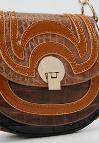 Brązowa i czarna tłoczona skórzana torebka z błyszczącymi, brązowymi szwami i okrągłym złotym zapięciem na przedniej klapie.