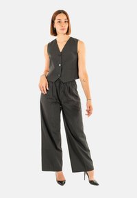 Gilet grigio a righe con scollatura a V e tre bottoni abbinato a pantaloni grigi larghi e a vita alta. Tacchi neri.