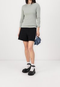 Žena na sobě má světle šedý dlouhý rukáv, černé kraťasy, bílé ponožky, černé platformové boty a drží malou modrou kabelku.