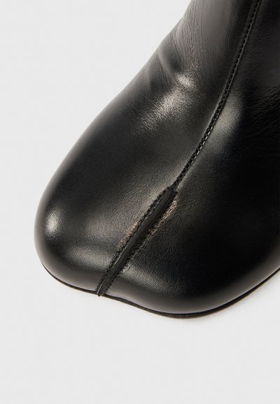 Černá kožená kotníková bota s špičatou špičkou, bezšvovým provedením a jemným leskem. Obsahuje viditelný šev po straně.