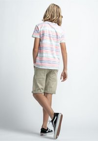 T-shirt à manches courtes rayé dans des couleurs pastel, associé à un short kaki. Baskets noir et blanc avec des semelles texturées.