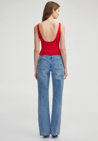 Top rojo sin mangas con un escote trasero profundo, combinado con jeans de pierna ancha de tiro alto, en un tono azul claro, con dobladillo deshilachado y dos bolsillos traseros.