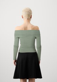 Grön off-shoulder-top med långa ärmar, figursydd överdel och rynkad textur, matchad med en svart utsvängd kjol.