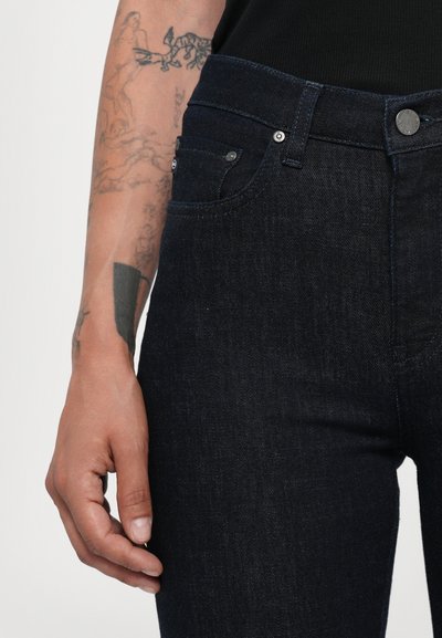 Dunkelblaue Jeans aus Denim mit einem enganliegenden Design, im Fünf-Taschen-Stil und metallischen Details am Bund. Glatte Textur und saubere Verarbeitung.