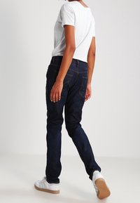 Mörkblå denimjeans med en smal passform, bakfickor, kombinerat med en ljusgrå t-shirt och vita sneakers med en beige sula.