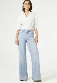 Jean en denim bleu clair taille haute à jambes larges, avec poches, fermeture à bouton et ourlet propre. Assorti à une chemise blanche à boutons.
