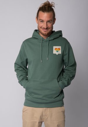 Green hoodie made of soft fabric, featuring a front pocket and an emblem with a rainbow heart. Drawstrings and ribbed cuffs complete the design.