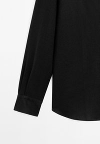 Detail van de manchetten en onderste mouwen van een zwarte lange mouwen shirt, weergegeven tegen een witte achtergrond.