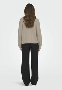Lichtbeige gestructureerde trui met een relaxed fit, gecombineerd met hoge zwarte wijde broek, bekeken vanuit de achterkant.