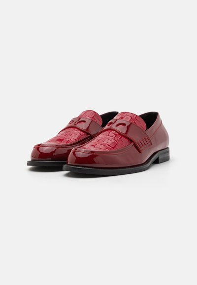 Röda lackläderloafers med texturerad framrem och dekorativa urtag, har en platt svart sula och rund tå.