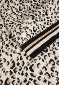 Maglione lavorato a maglia con una base crema e una stampa leopardata nera e marrone. Presenta polsini neri solidi con strisce orizzontali beige e nere.