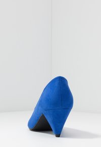 Chaussure à talon haut en daim bleu avec un bout pointu et un talon effilé. La chaussure présente une texture lisse et une semelle noire.