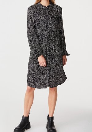Black and white patterned dress with long sleeves, collar, and buttons; knee-length, made of lightweight fabric, paired with black ankle boots.