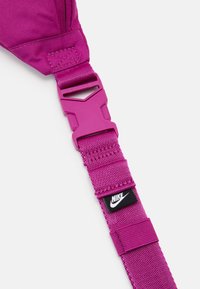 Regulowany pasek Nike w jaskrawym różowym kolorze, wykonany z teksturowanego nylonu, z plastikową klamrą i małą czarną metką z logo marki.