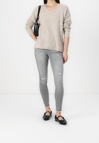 Pull beige en maille à col en V, associé à un jean skinny gris clair déchiré et des ballerines noires ornées de décorations.