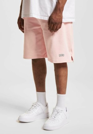 Lichtroze katoenen shorts met zijslits, voorzien van een kleine bedrukte logo "DEF" op de zoom, gecombineerd met witte sneakers en sokken.