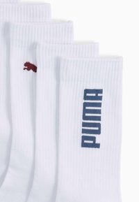 Białe skarpetki do kostek z prążkowaną teksturą. Jedna skarpetka ma czerwone logo Puma, a druga niebieski tekst "PUMA", oba umieszczone z boku.