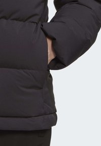 Black puffer jacket with a high collar, featuring a textured exterior and a side pocket. The fabric appears thick and plush.
