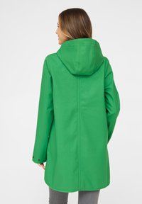 Chaqueta verde impermeable con capucha, textura suave, mangas largas y detalles de botones a presión en las muñecas. Vista trasera mostrada.