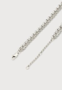 Ασημένιο κολιέ με στρωματοποιημένες αλυσίδες, τρεις διαφορετικοί τύποι κρίκων και κούμπωμα τύπου αστακού σε λευκό φόντο.