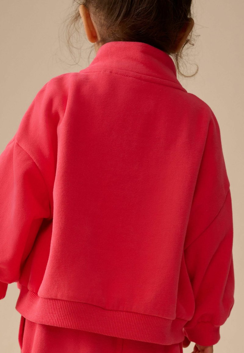 Sweat-shirt rose vif avec un col montant, coupe ample, poignets et ourlet côtelés. Texture lisse avec des coutures minimales, vu de dos.